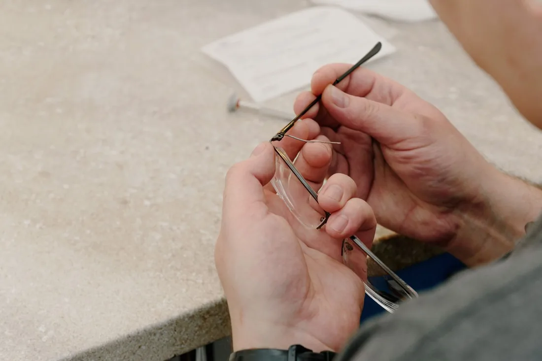 Manos sobre una mesa de taller uniendo con un destornillador la varilla al frente de una montura de gafas